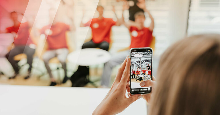 Im Vordergrund ist ein Handy, mit dem sechs Personen im Hintergrund fotografiert werden.