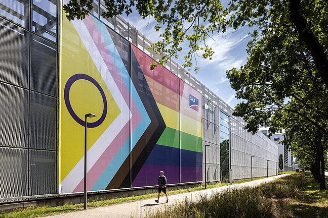 Man sieht eine große Pride-Flagge, die von außen an einem Parkhaus befestigt ist.